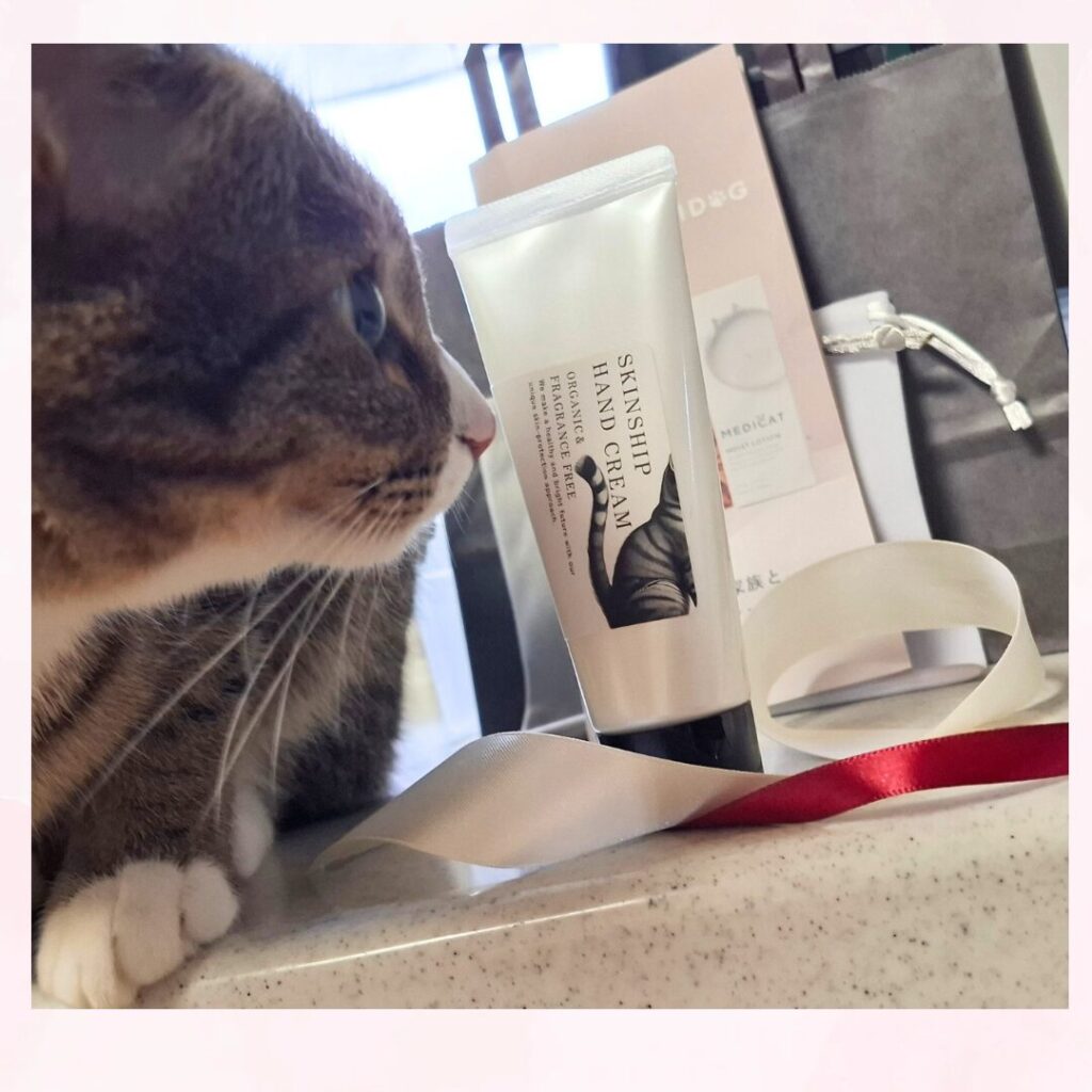 レオが スキンシップ ハンドクリームの容器に 鼻先をつけようとしている。後ろには 注文時に一緒に入っていたブランド商品の用紙