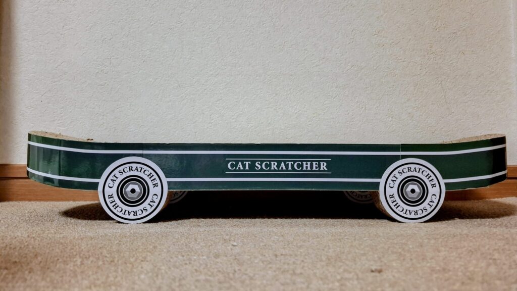 「CAT SCRATCHER」というロゴが入った、緑色のスケートボード型猫用爪とぎ。真横から撮影され、爪とぎの下に空間が作られていることがわかる。